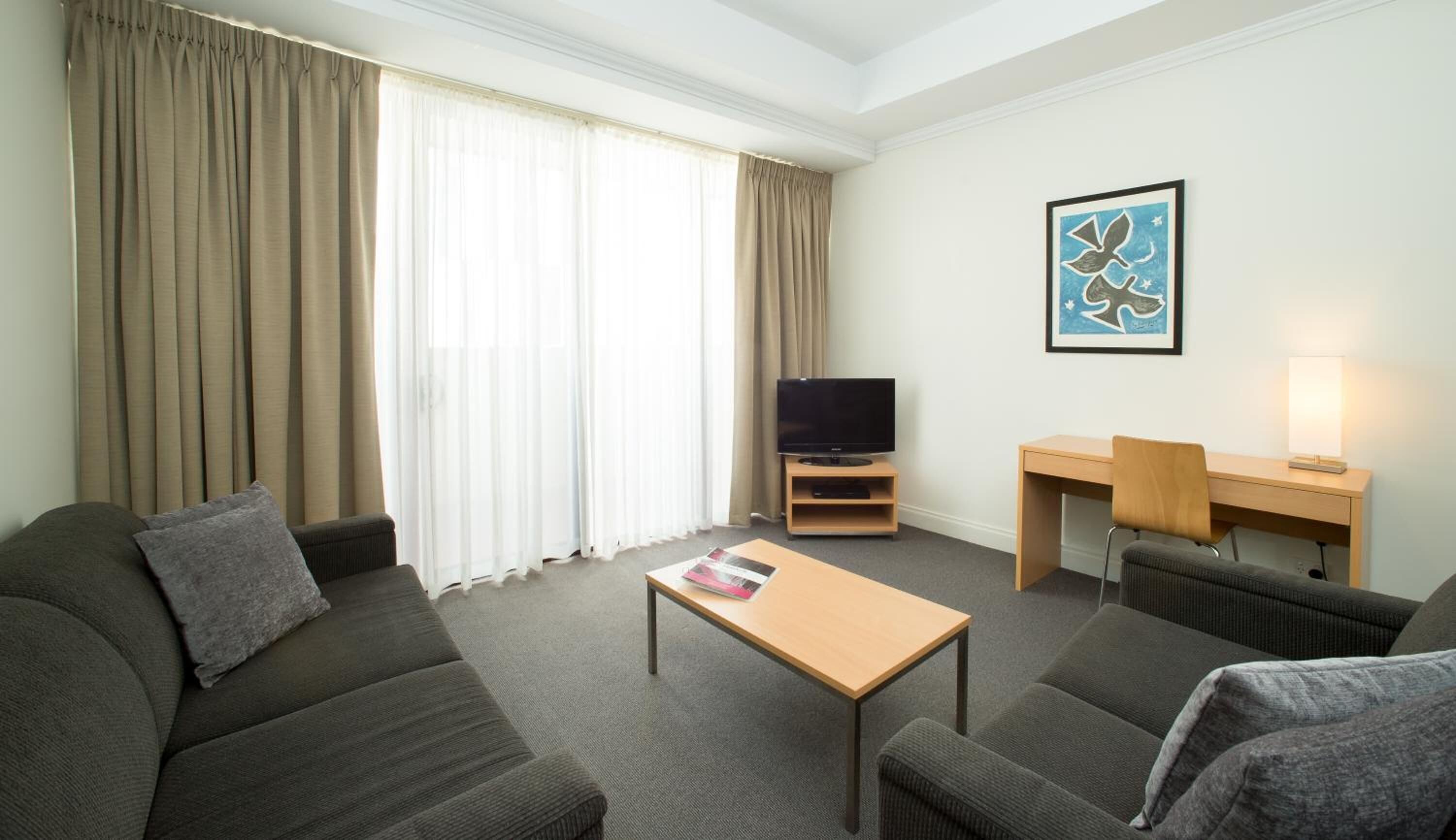 A hotel room with a sofa, a small table, a TV, a desk, and a lamp.