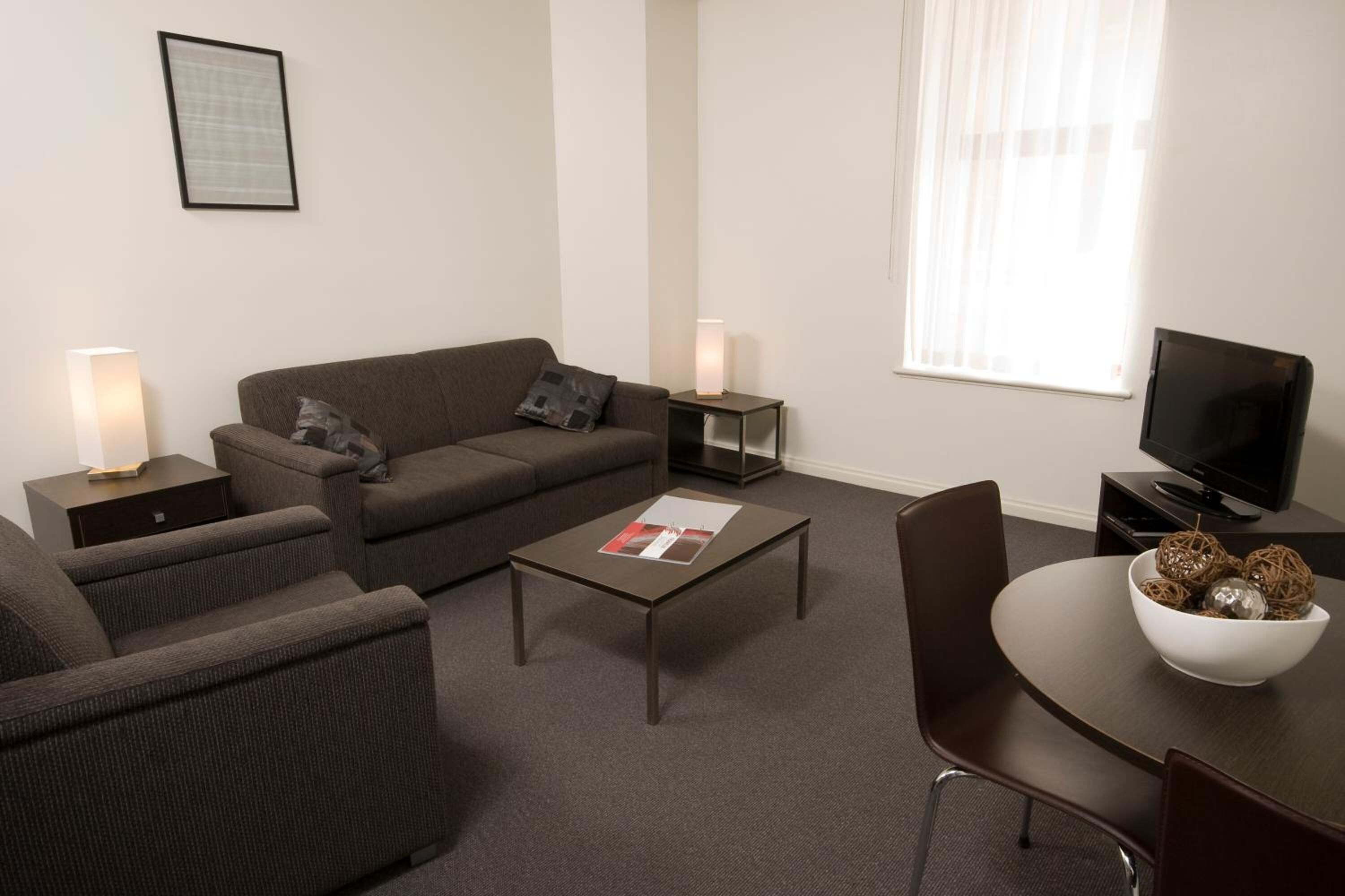 Una sala de estar moderna con sofá, sillón, mesa de centro, televisor y una mesa de comedor con un cuenco de adornos.