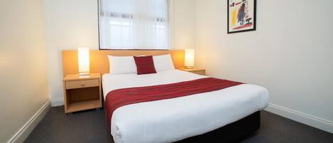 A hotel room with a large bed, two bedside tables with lamps, a window with sheer curtains, and a framed picture on the wall.