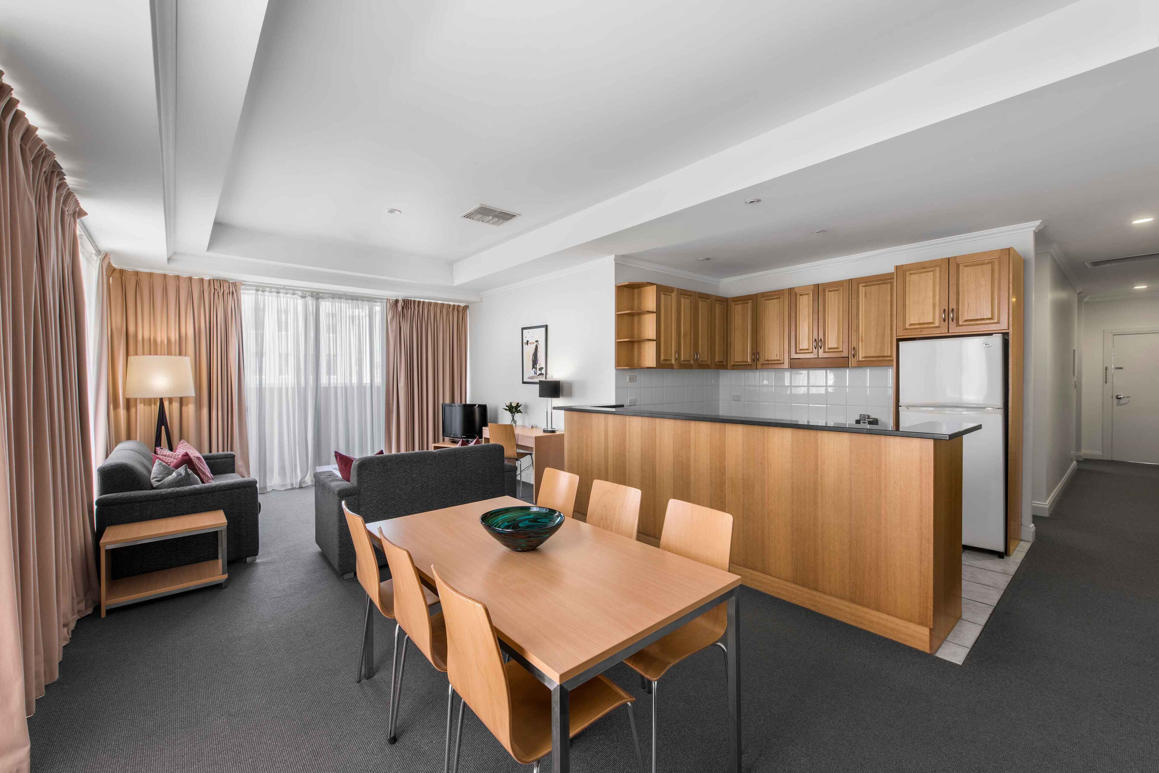 A modern hotel room with a dining area, kitchenette, and a living space.
