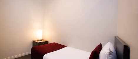 Una habitación de hotel con una cama individual, una mesita de noche con lámpara y una manta roja.