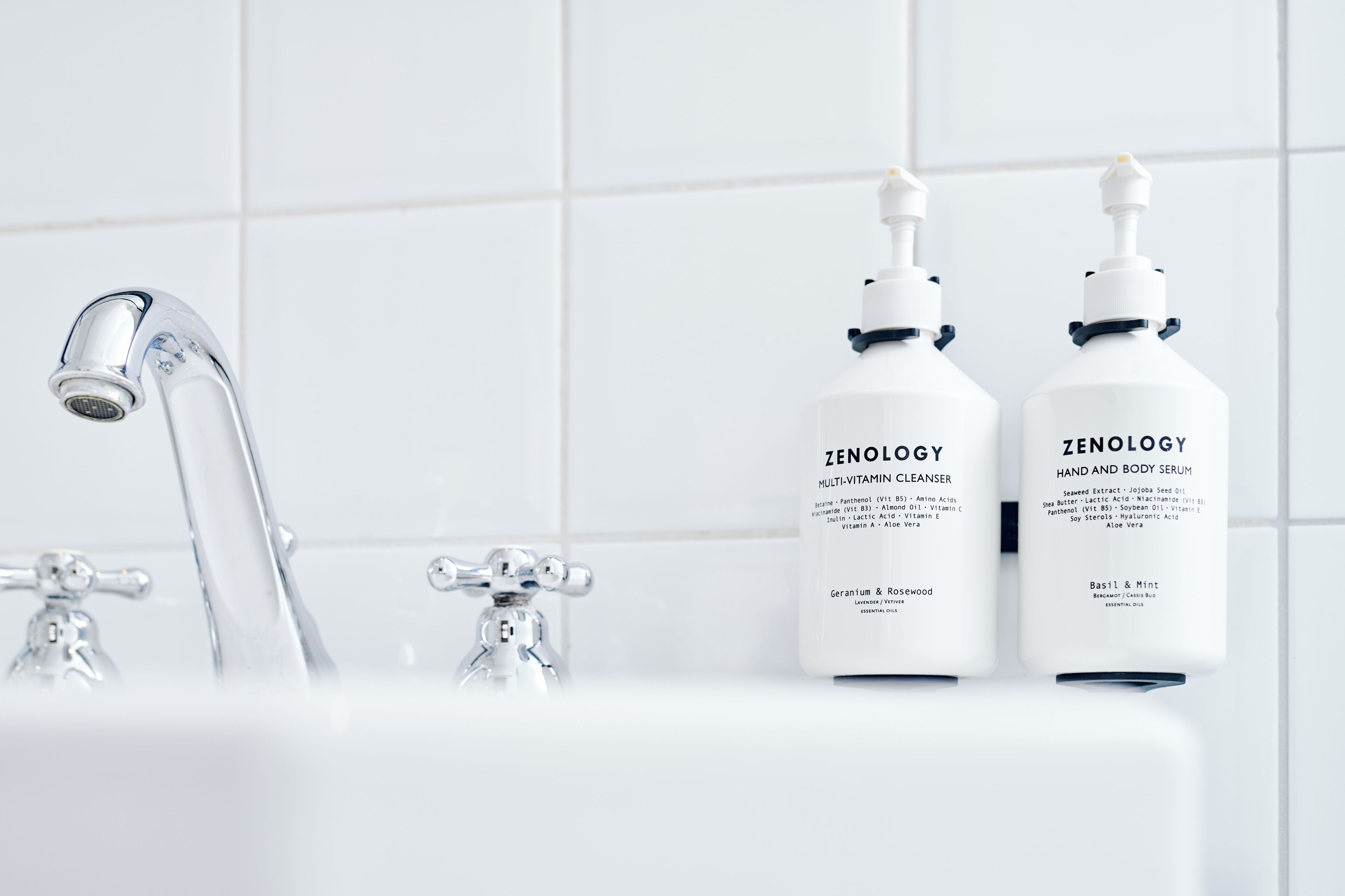 A bathroom with a modern faucet and two bottles of Zenology hand and body serum.