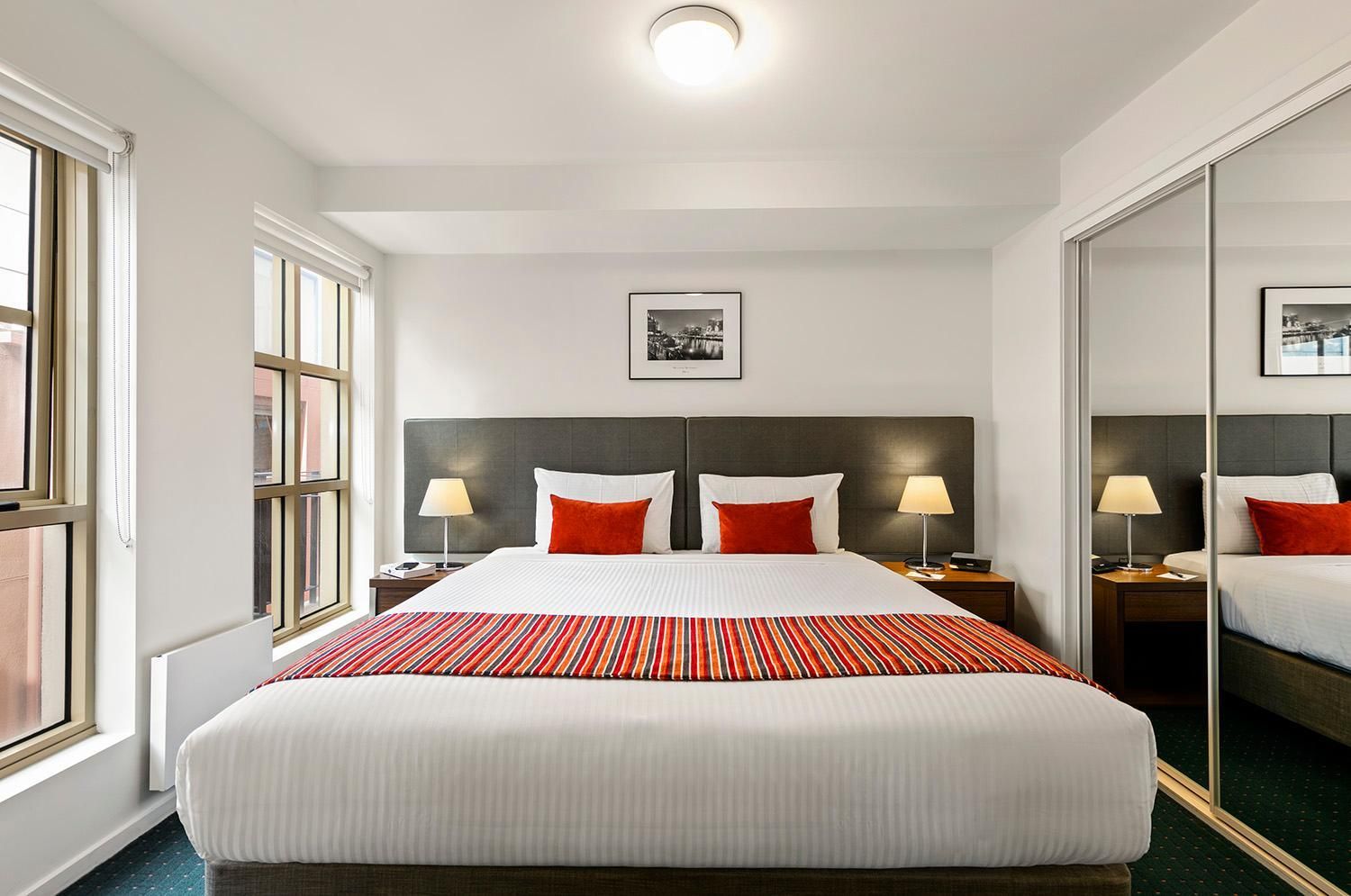 A hotel room with a large bed, two bedside tables with lamps, a framed picture on the wall, and a mirror on the door.