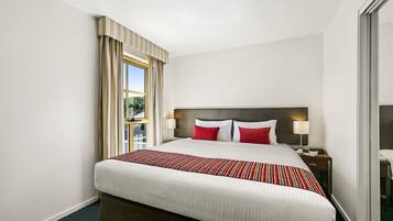 Habitación de hotel con una cama grande, una mesita de noche con lámpara, una ventana con cortinas y vistas al exterior.
