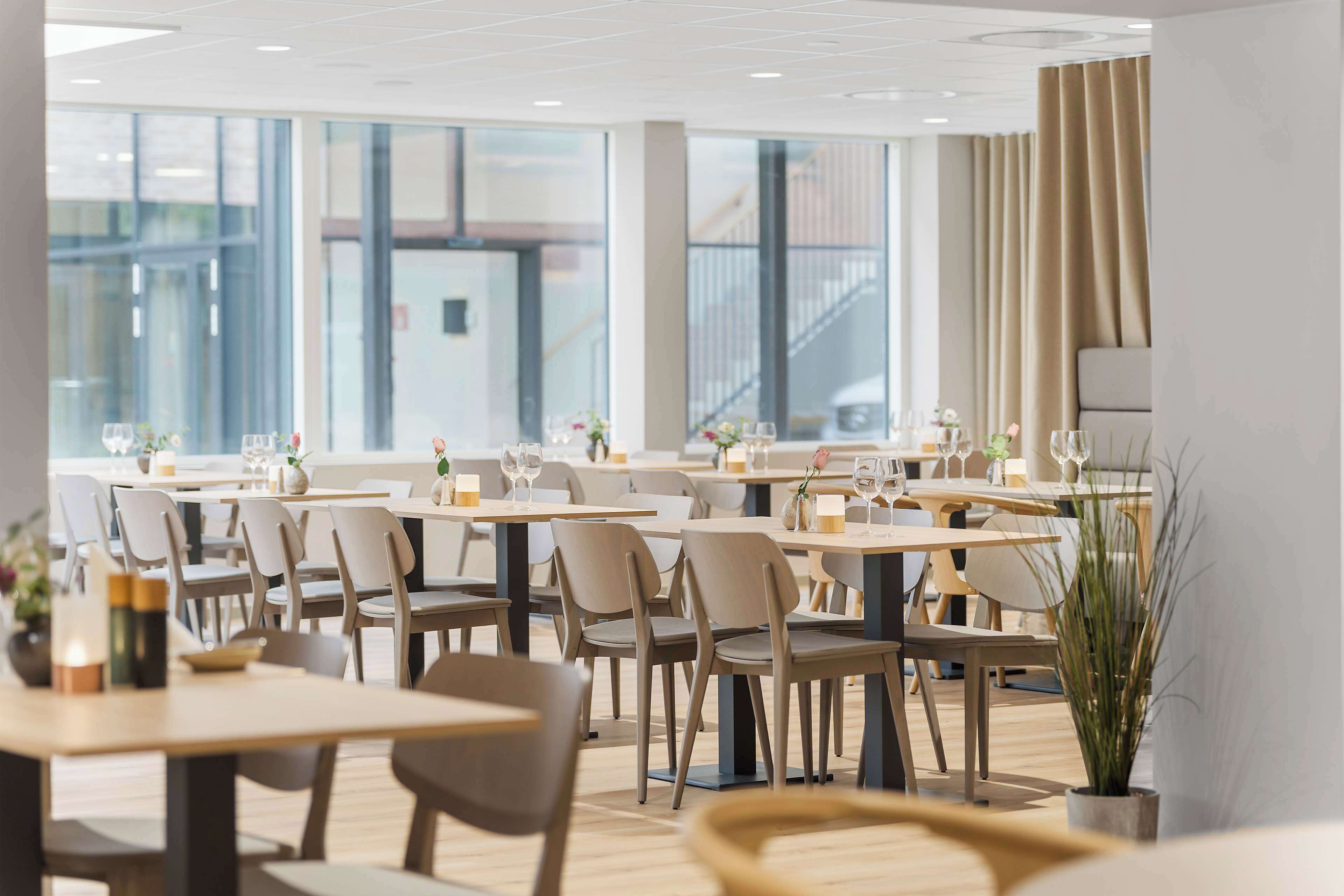 Et moderne spiseområde med flere borde og stole, store vinduer og udsigt over byen.