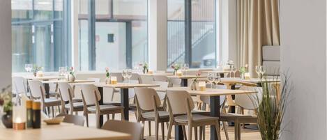 A modern dining area with multiple tables and chairs, large windows, and a view of the city.