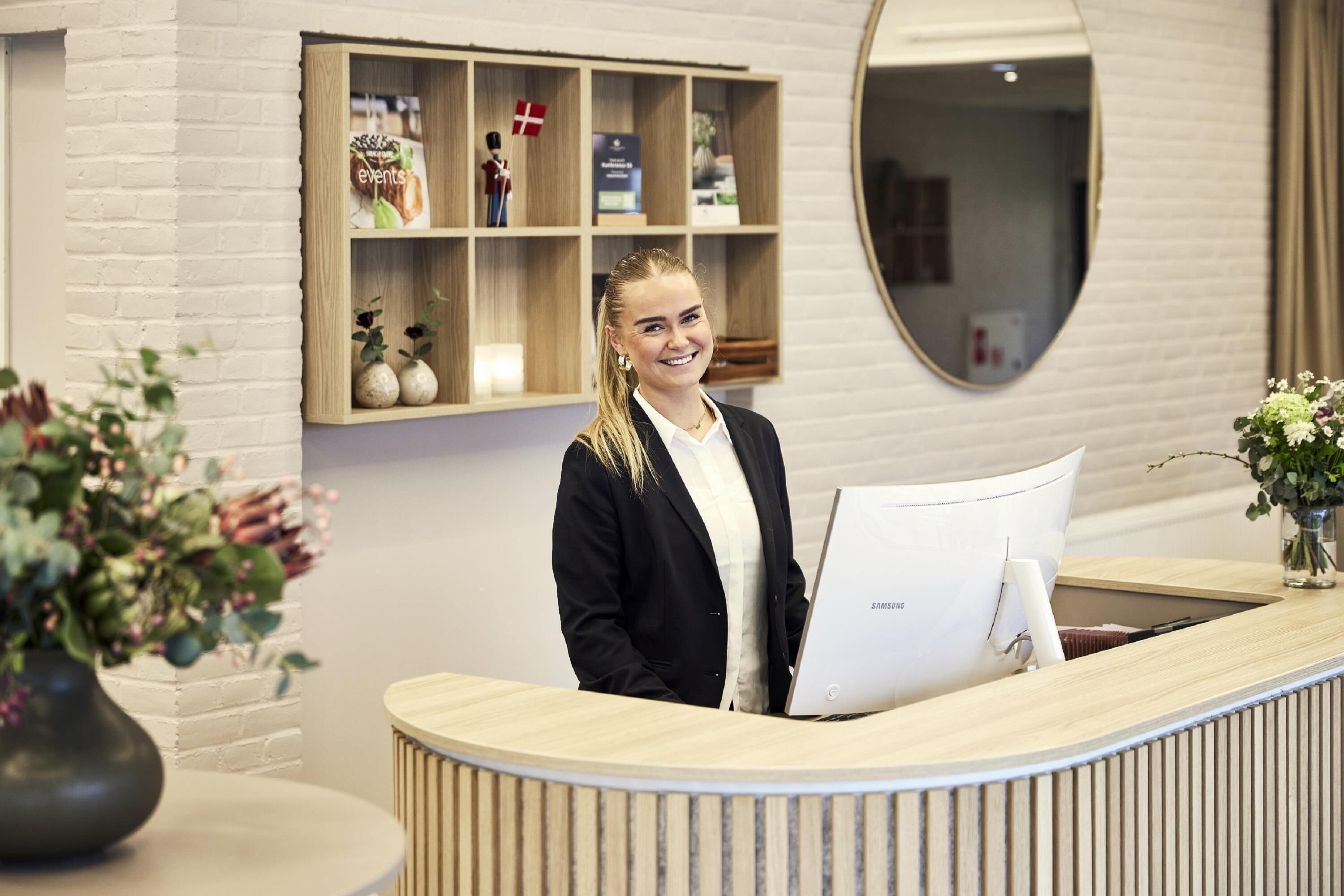 Un comptoir d’accueil avec un écran Samsung, une étagère en bois ornée d’objets décoratifs et un miroir au-dessus.