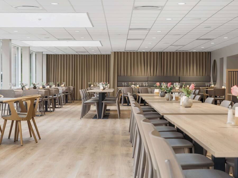 A modern dining area with long tables and chairs, a wooden floor, and a large wall with a vertical panel design.