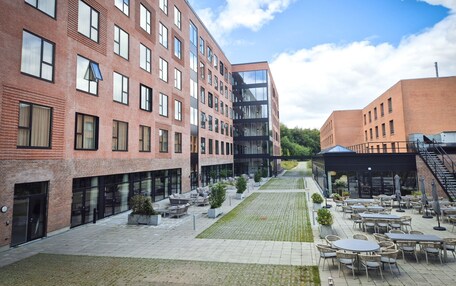 A courtyard with outdoor seating, a modern building with large windows, and a brick facade.