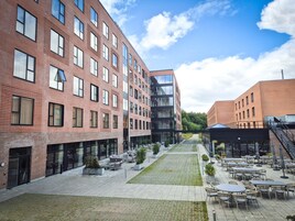 En gårdhave med udendørs siddepladser, en moderne bygning med store vinduer og en murstensfacade.