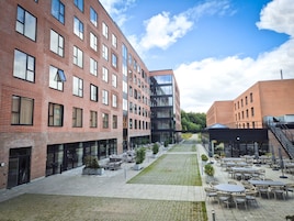 En gårdhave med udendørs siddepladser, en moderne bygning med store vinduer og en murstensfacade.