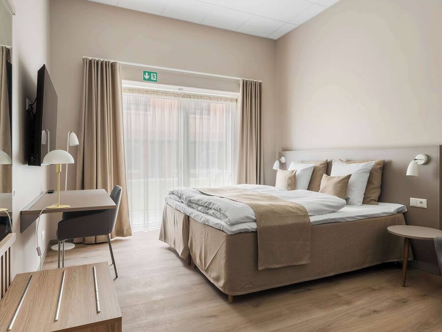 Una habitación de hotel con cama, mesita de noche, escritorio, silla y televisor.