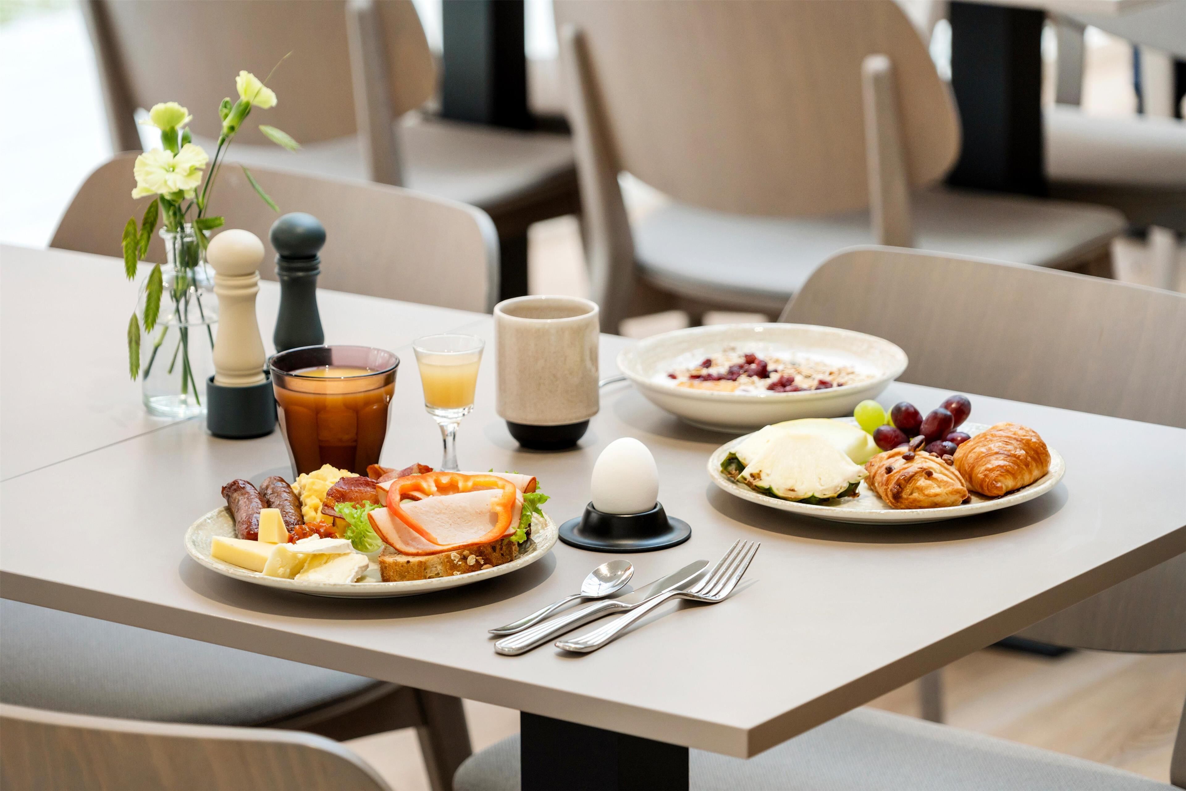 Et morgenbord med tallerkener med mad, en kaffekop, salt- og peberkværn og en vase med blomster.