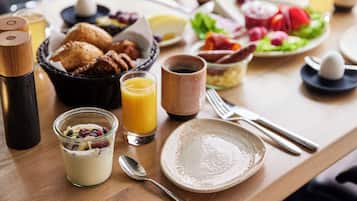 Una mesa de desayuno con diferentes alimentos, un vaso de jugo de naranja y una taza de café.