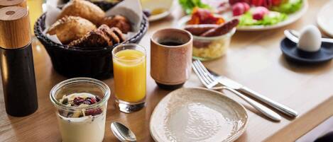Una mesa de desayuno con diferentes alimentos, un vaso de jugo de naranja y una taza de café.