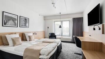 A hotel room with a bed, a desk, a chair, a TV, and two framed pictures on the wall.