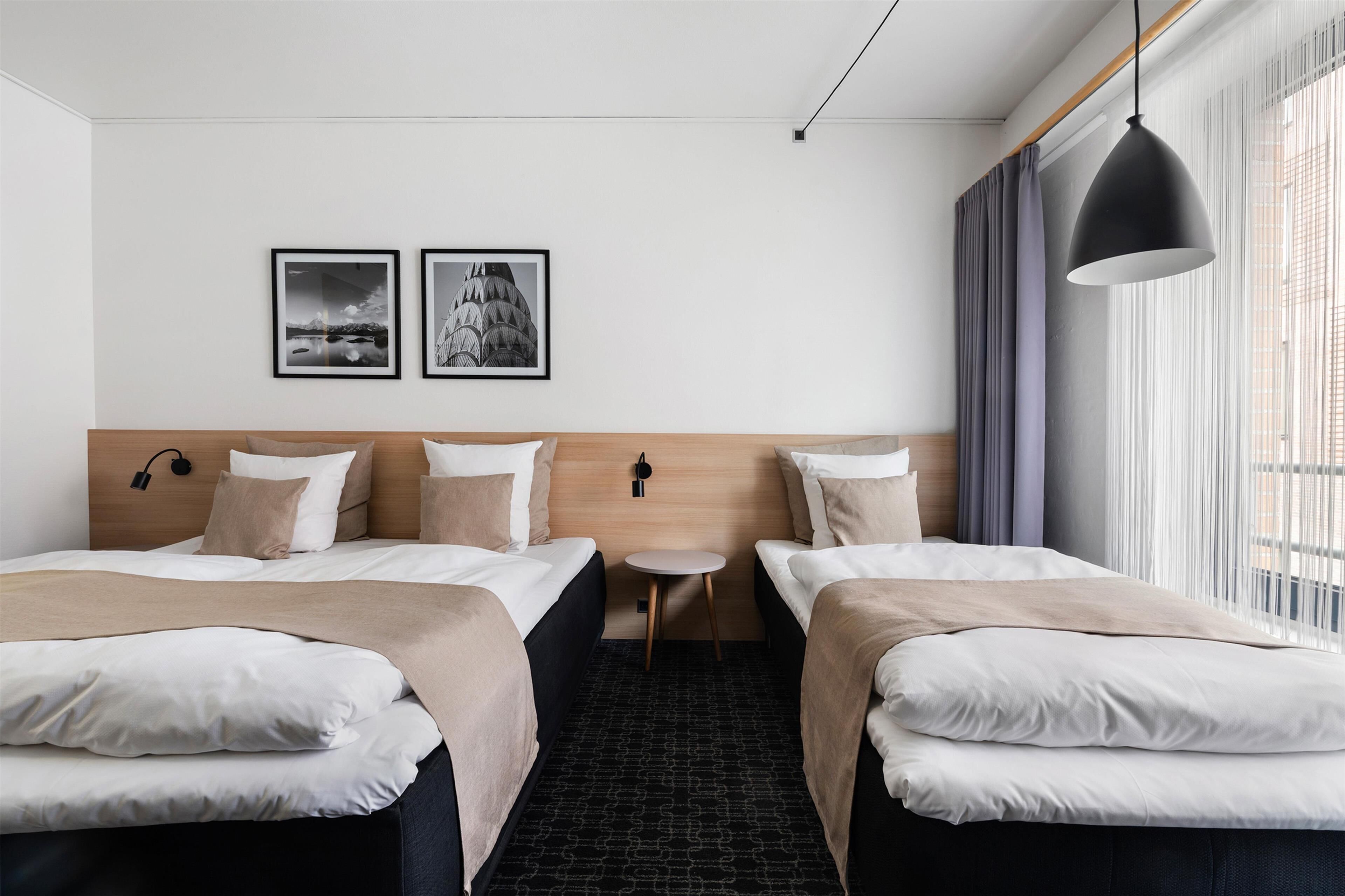 A hotel room with two beds, a small round table, and two framed pictures on the wall.
