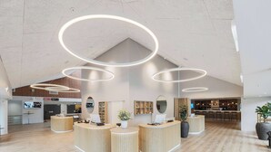 A modern reception area with wooden reception desks, a bar in the background, and a high ceiling with circular light fixtures. - Best Western Plus Hotel Odense (Odense)