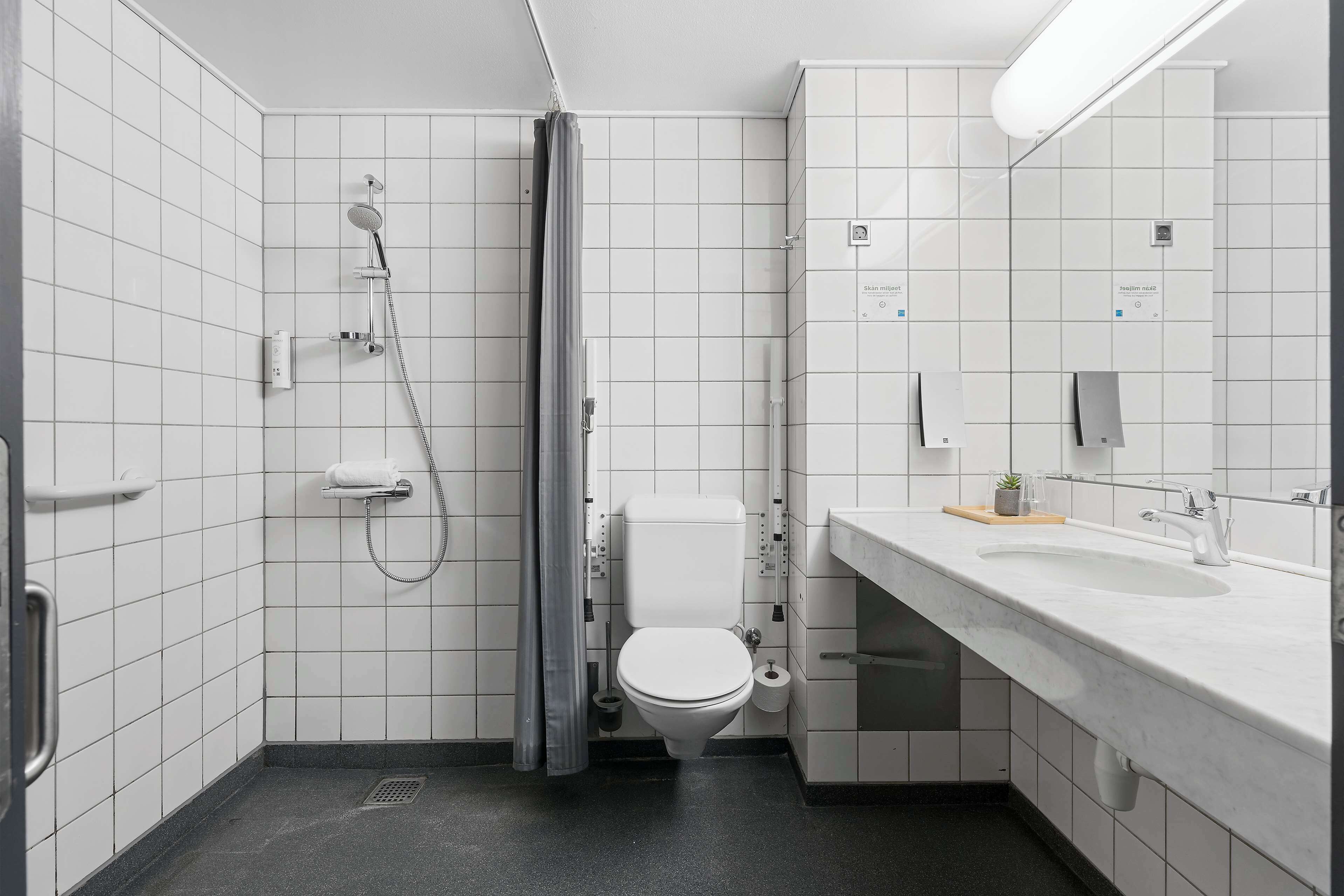 Une salle de bain moderne avec des carreaux blancs, des toilettes, une douche, un lavabo et un miroir.