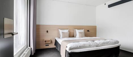 Una habitación de hotel moderna con una cama grande, una mesita de noche, un estante empotrado y un ventanal con cortinas.