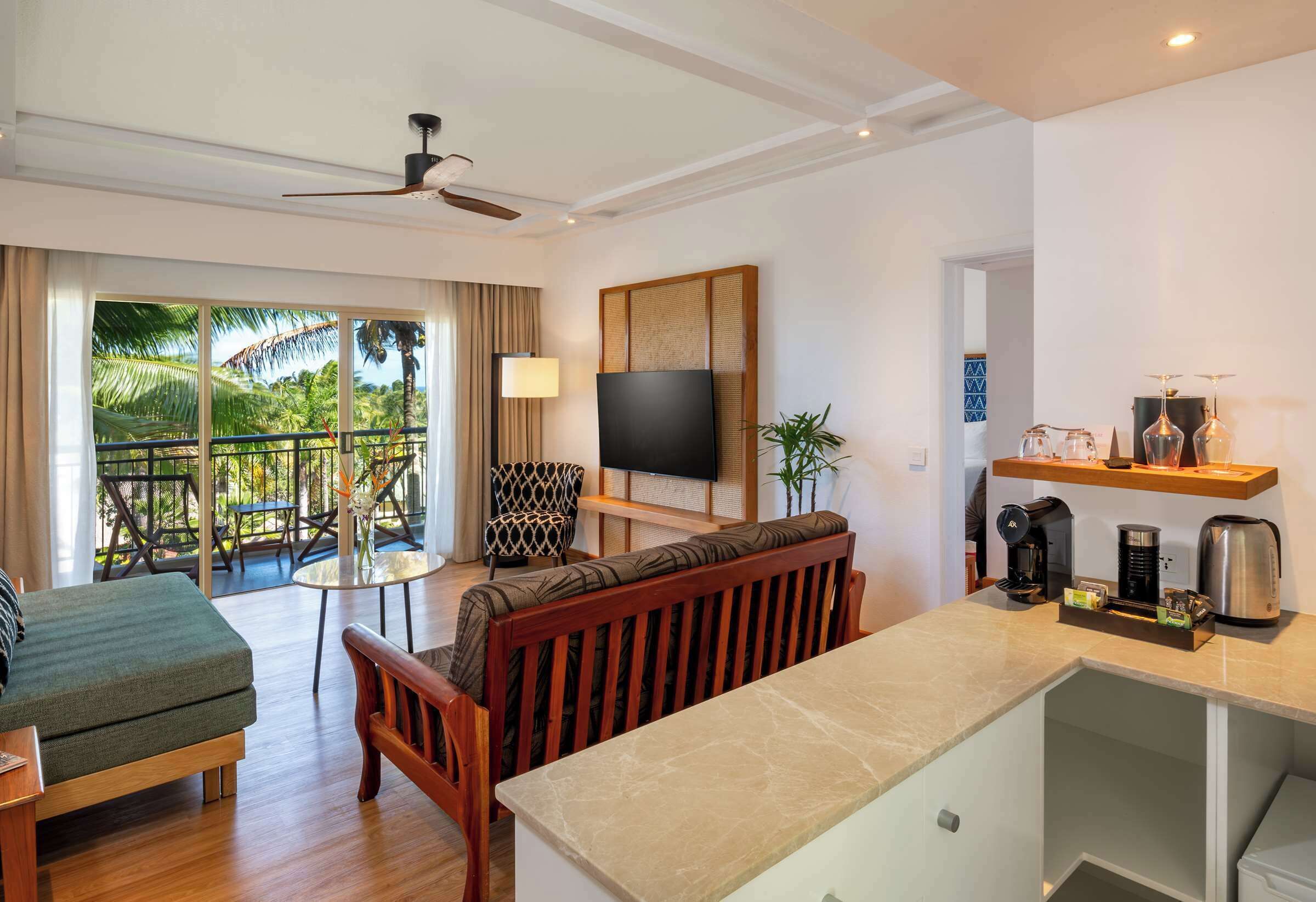 A hotel room with a balcony, a sofa, a TV, a coffee maker, and a small table.