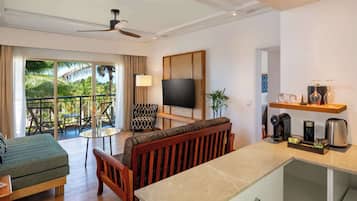 A hotel room with a balcony, a sofa, a TV, a coffee maker, and a small table.