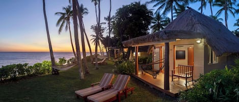 A beachfront property with a thatched-roof structure, lounge chairs, and a view of the ocean.
