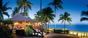 A beachside restaurant with a thatched roof, palm trees, and a view of the ocean. - OUTRIGGER Fiji Beach Resort (Korotogo)