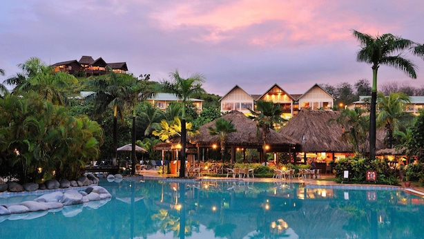 Un resort con piscina, construcciones de techo de paja y exuberante vegetación.