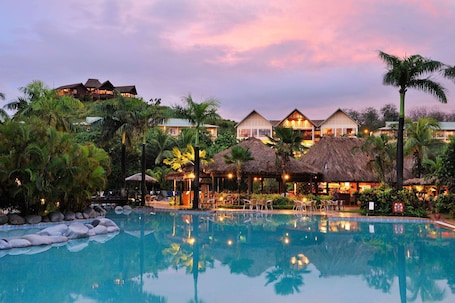 A resort with a swimming pool, thatched-roof structures, and lush greenery.