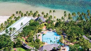An aerial view of a resort with a swimming pool, palm trees, and a beach.