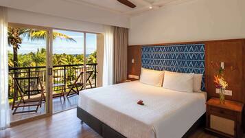 A hotel room with a large bed, a balcony with chairs, and a view of palm trees.