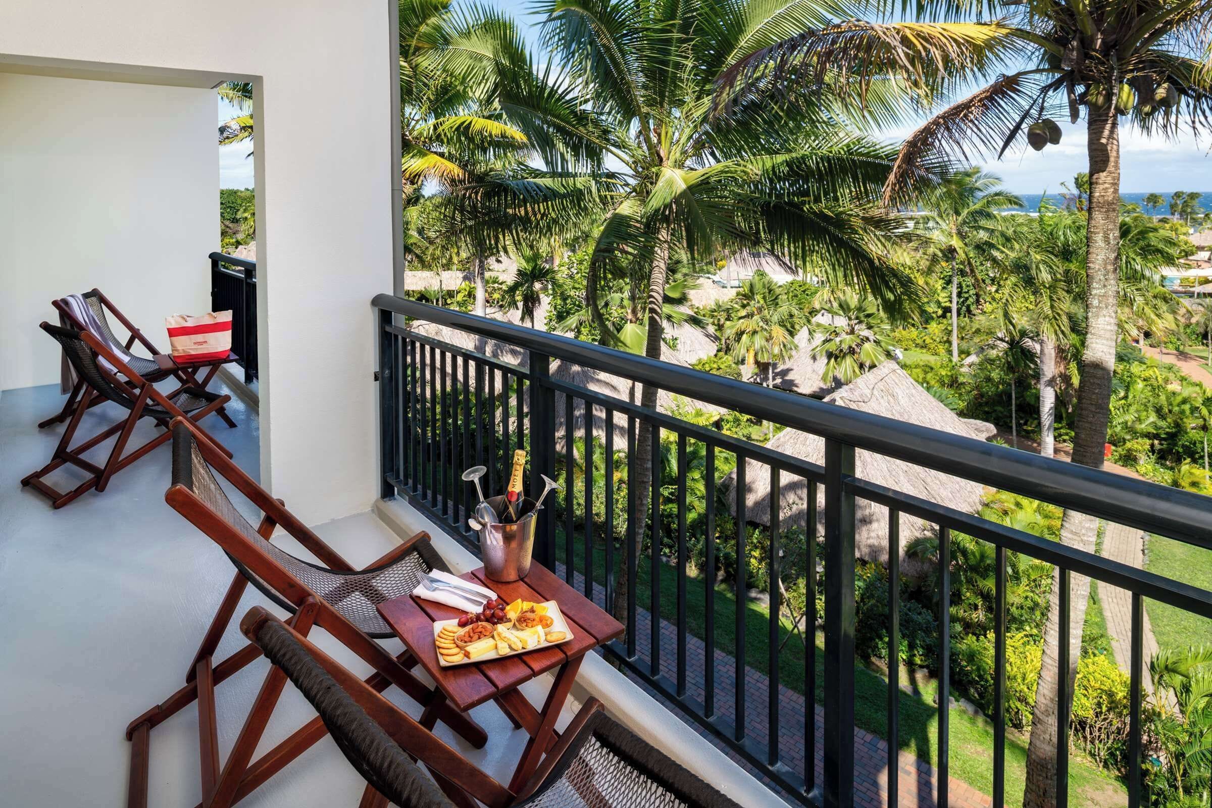 A balcony with wooden chairs, a table with a plate of food, and a metal bucket with utensils.