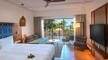 A hotel room with a bed, a sofa, a TV, a ceiling fan, and a view of the outdoors.