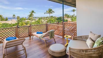 A balcony with wicker furniture, a round ottoman, and a view of the beach and palm trees.