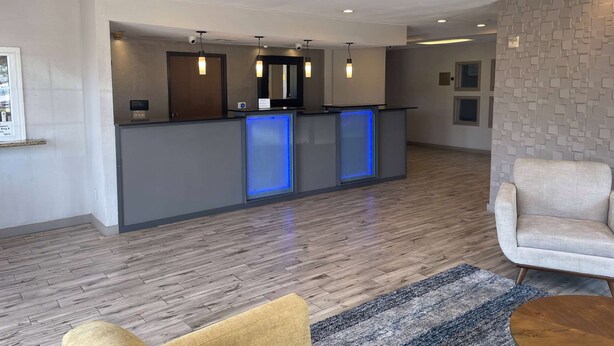 A modern reception area with a wooden floor, a reception desk with blue backlit panels, and a seating area with a sofa and armchair. - Days Inn by Wyndham Mesquite Rodeo TX (Mesquite)