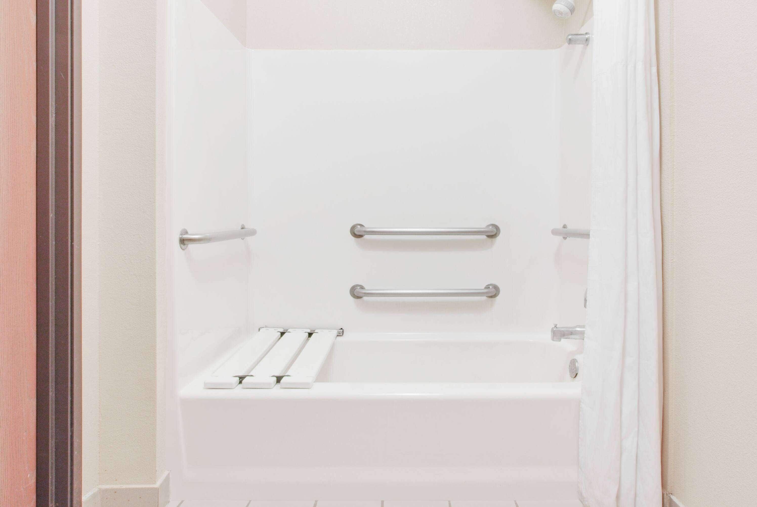 A white bathtub with two grab bars and a shelf.