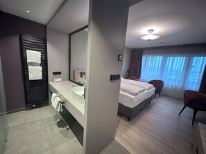 Een moderne hotelkamer met een groot bed, een badkamer met een wastafel en spiegel, en een zithoek met een stoel.