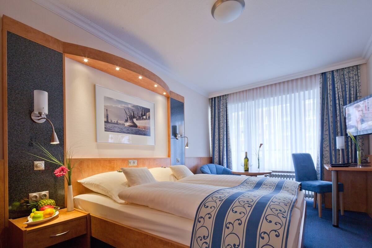 Een hotelkamer met twee bedden, een bureau, een stoel, een televisie en een raam met gordijnen.