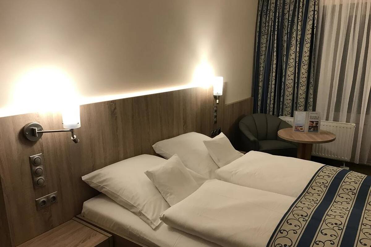 Een hotelkamer met een opgemaakt bed, een nachtkastje, een stoel en een kleine tafel met een menukaart.