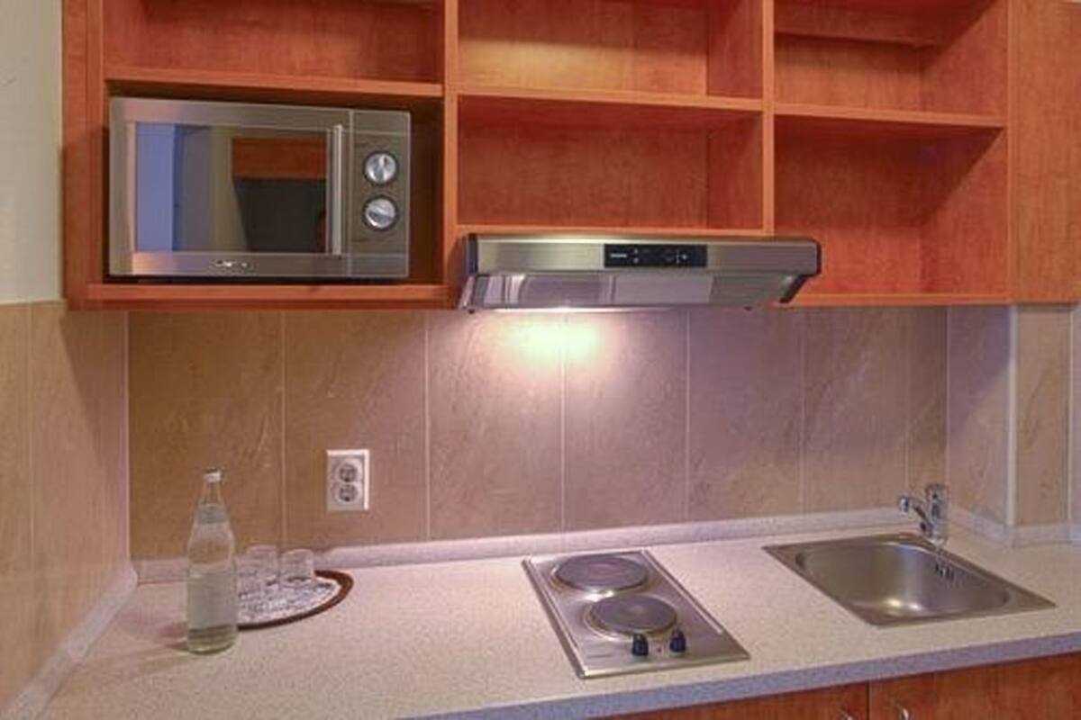 Een kleine keuken met een magnetron, fornuis en spoelbak.