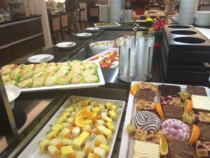 Een buffet met diverse soorten eten, zoals belegde broodjes, fruit en desserts.