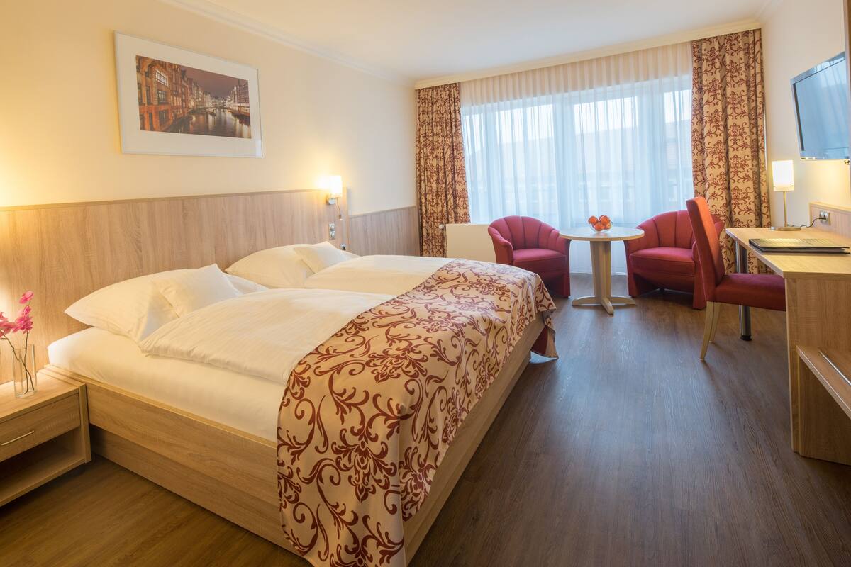 Hotelkamer met een groot bed, twee stoelen, een klein tafeltje, een televisie en een stadsgezicht aan de muur.