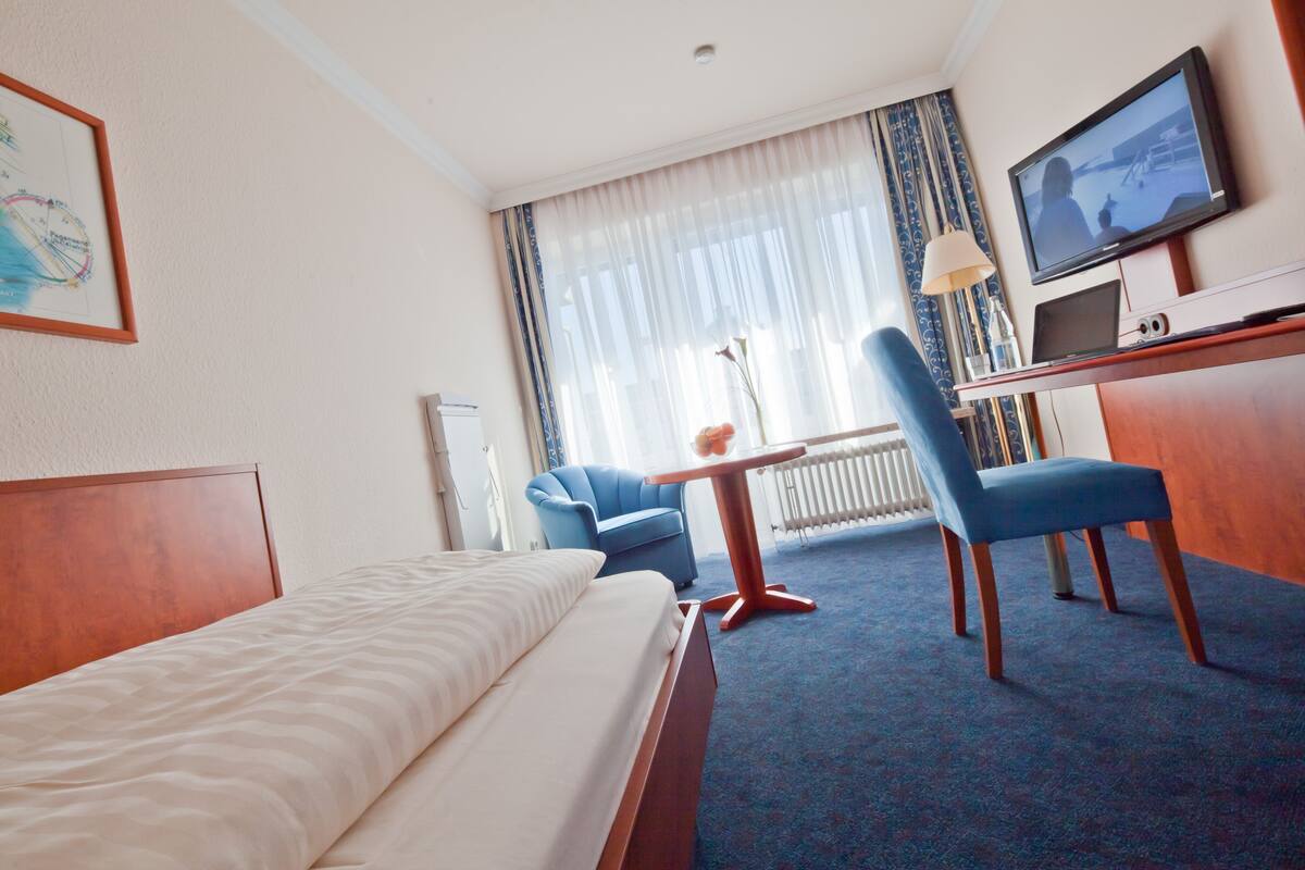 Een hotelkamer met een bed, een bureau met een televisie, een stoel en een raam met gordijnen.