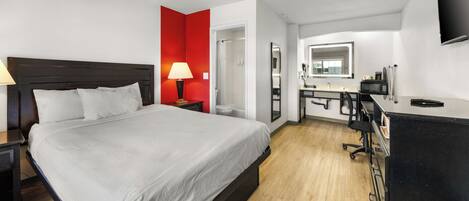 A hotel room with a large bed, a desk with a computer, a mirror, and a TV.