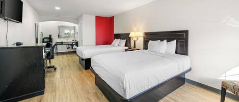 A hotel room with two beds, a desk, a TV, and a red accent wall.
