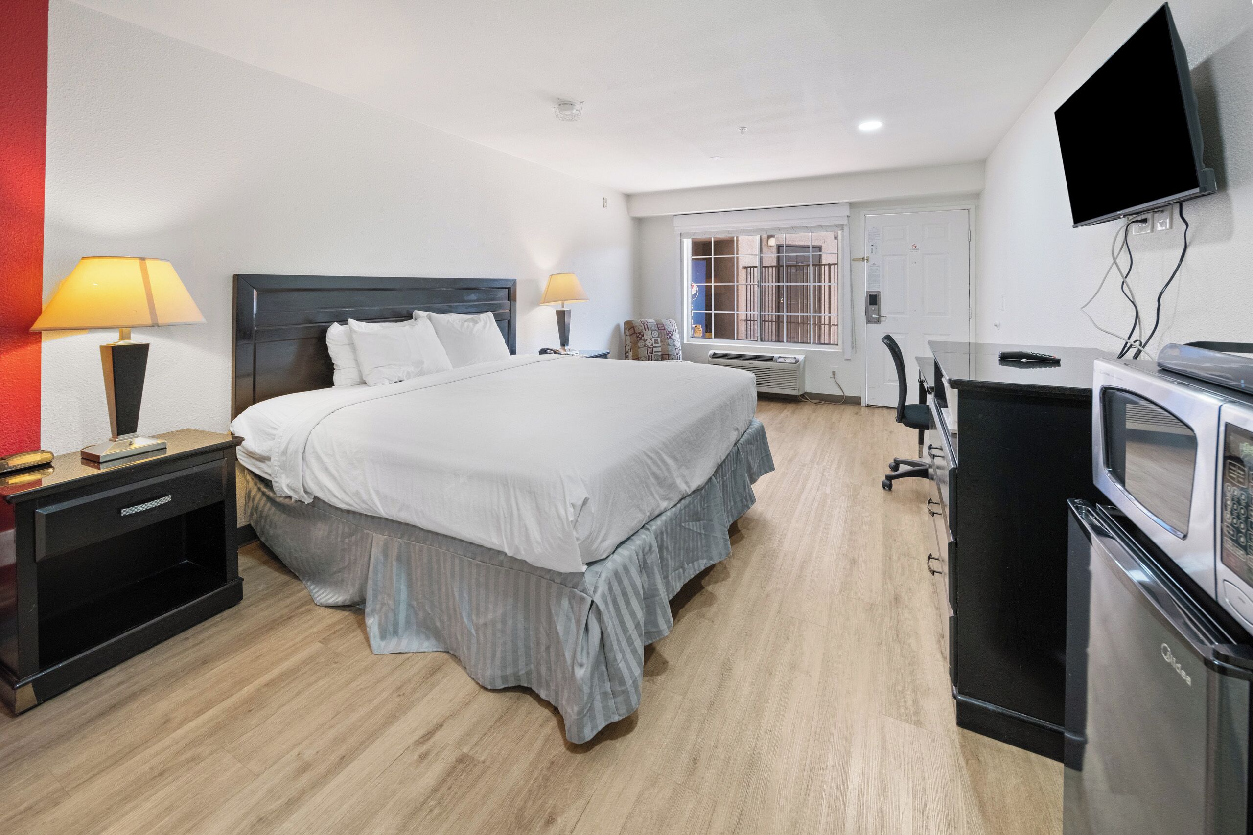 Hotelkamer met groot bed, nachtkastjes met lampen, bureau met stoel, televisie aan de wand en een magnetron.