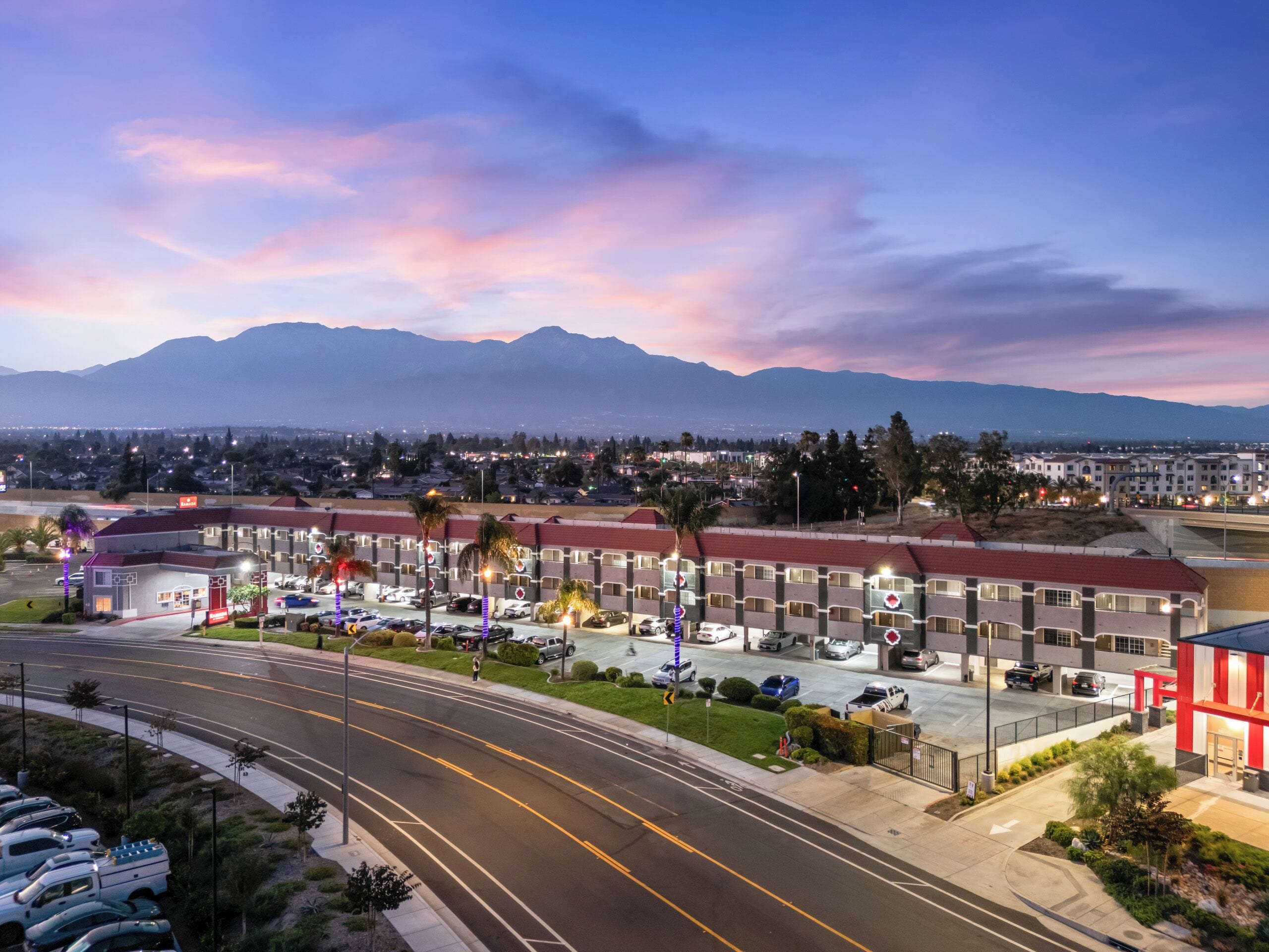 A hotel with multiple parking levels, a red building, and a view of mountains in the background.