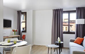 Relax in a stylish room with a sofa, dining table, and flat-screen TV, offering a city view through large windows.