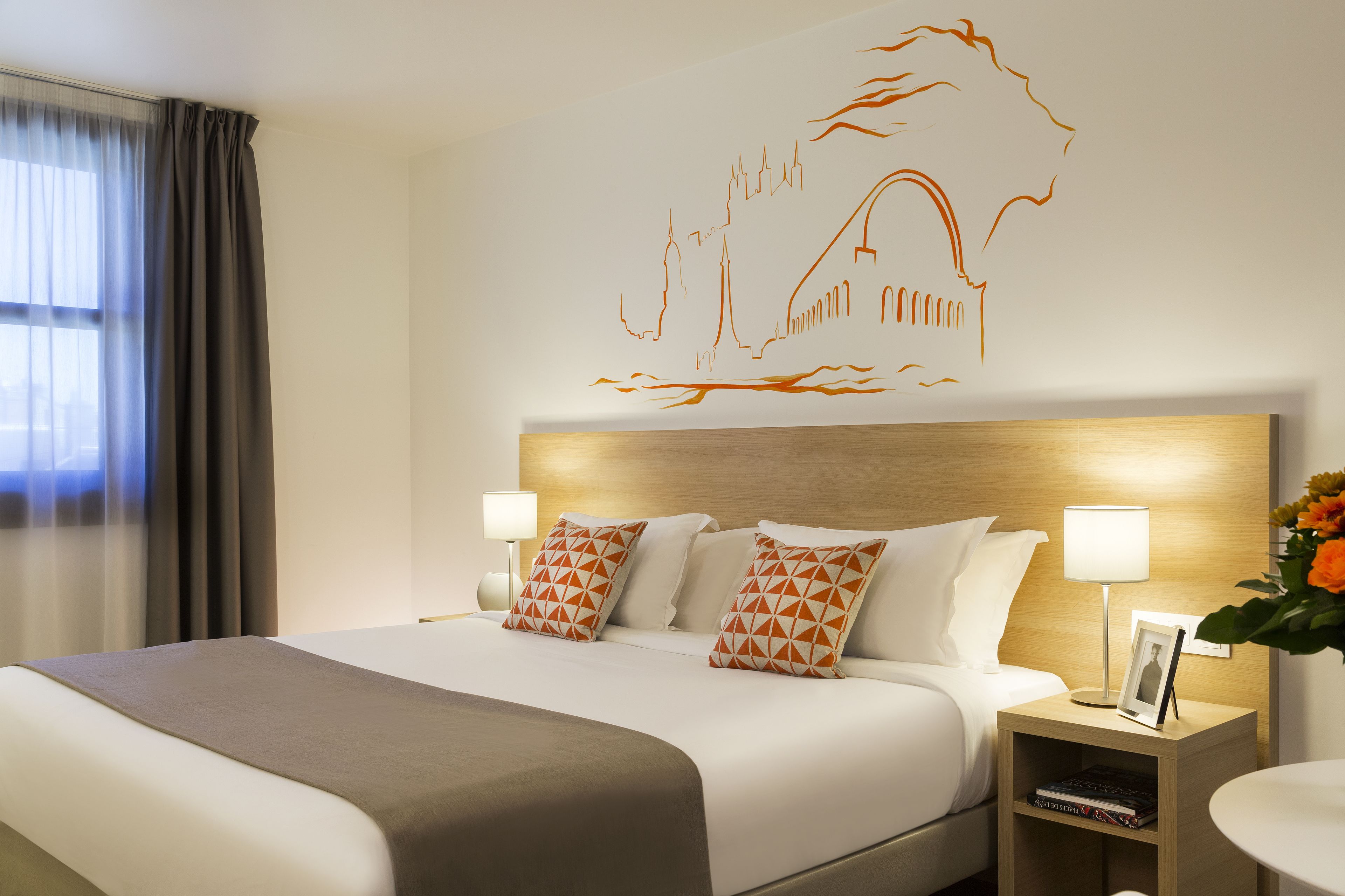 A hotel room with a large bed, two bedside tables with lamps, a wall art piece, and a window with curtains.